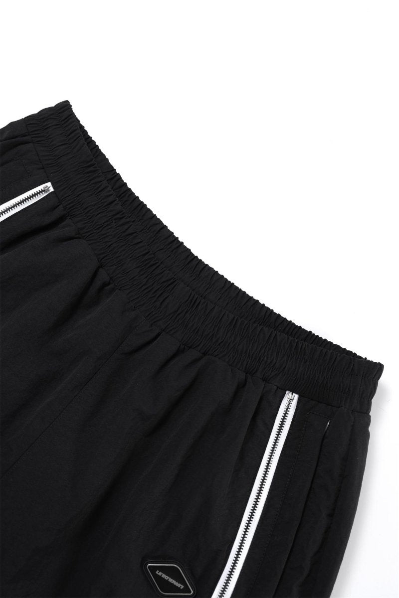 Black and white NPT Baby Gang zip track pants showcasing elastic waistband and zipper details.