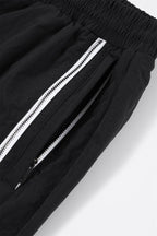 Close-up of black and white NPT Baby Gang zip track pants showcasing the zippered pockets and elastic waistband.