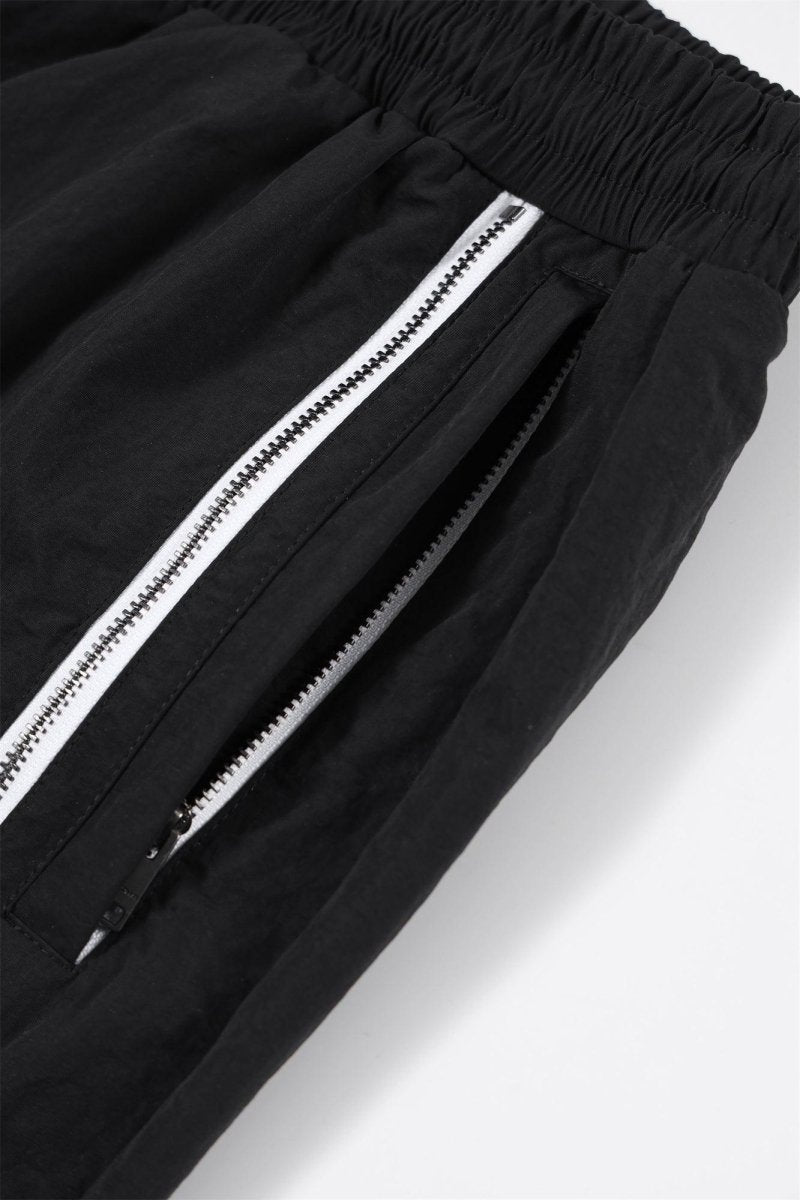 Close-up of black and white NPT Baby Gang zip track pants showcasing the zippered pockets and elastic waistband.