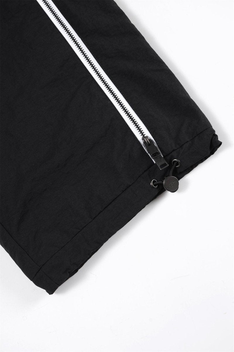 Close-up of the black ankle area of Black / White NPT Baby Gang Zip Track Pants with zip detail.