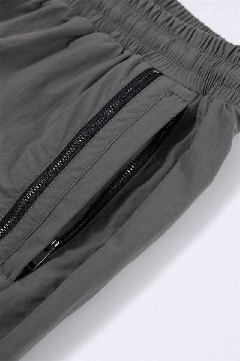 Close-up of grey NPT Simba La Rue zip track pants showing elastic waistband and zippered pocket details.